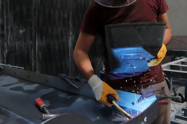 Sheet metal worker welding a custom metal enclosure in a fabrication workshop